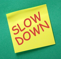 The words Slow Down in red text on a yellow sticky note as a reminder to take time out and avoid stress