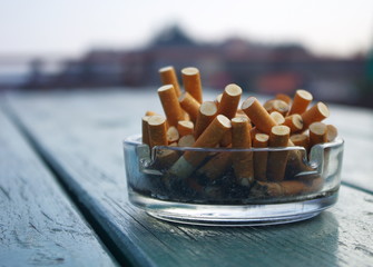 Ashtray full of cigarettes butts outdoor on green wooden table