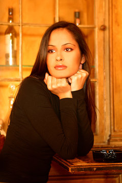 Bella donna in un locale con i pugni chiusi sul mento, guarda assorta verso fuori in un atmosfera molto calda e avvolgente