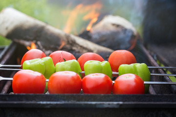 Grilling tomatoes and paprika on skewers with fire outdoors. Selective focus on paprika