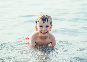 Fototapeta na wymiar Portrait of funny adorable smiling laughing white Caucasian one young little boy in water ocean sea, emotional active healthy lifestyle summer mood