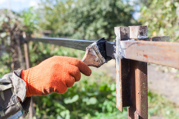 The man paints a black paint metal profile construction.