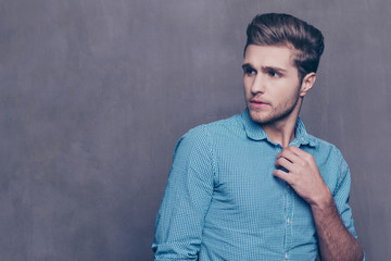 Thoughtful stylish man standing in front of gray background and touching his collar