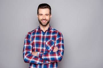 A photo of young man in checkered shirt with beaming smile posing against gray background