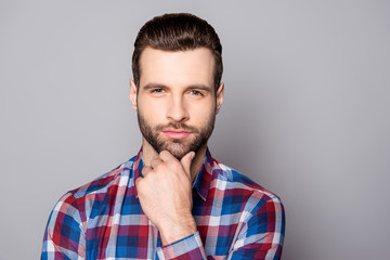 A close up portrait of young minded businessman touching his chin and standing against gray...
