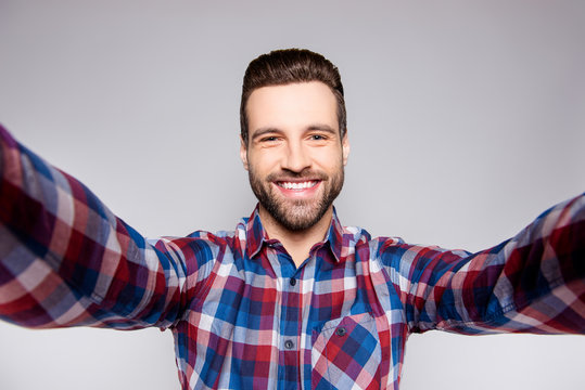Young satisfied cheerful man smiling and taking a selfie against gray background