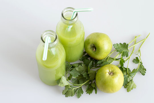  Source of natural vitamins. Glass bottles with fresh juice, green apples and sprigs of parsley on a light background.