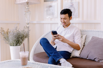 Obraz premium Asian man using a mobile phone and drink coffee in bakery shop