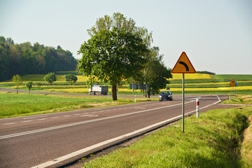 znak drogowy przy drodze mówiący o zakręcie  - obrazy, fototapety, plakaty