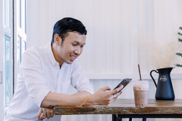 Asian man using a mobile phone and drink coffee in  bakery shop