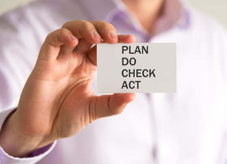 Businessman holding a card with PLAN DO CHECK ACT message