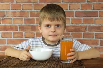 Cute little boy eating corn flakes on breakfast and drinking juice