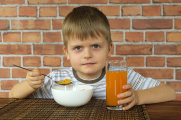 Boy with corn flakes and juice eating from wooden table