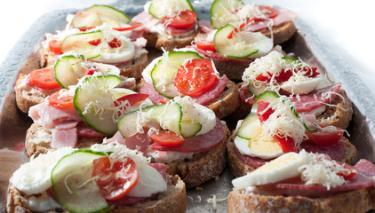 sandwiches with vegetables, ham and grated cheese on a tray