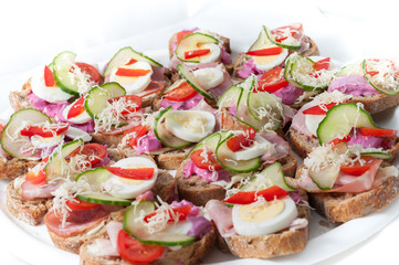 sandwiches with vegetables, ham and grated cheese on a tray