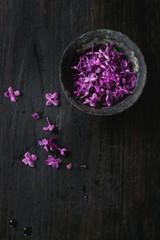 Vintage iron bowl of edible lilac flowers over black wooden background. With copy space. Top view