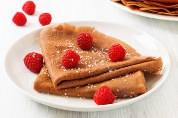 Chocolate crepes with fresh raspberries on white plate and cup of tea and coffee