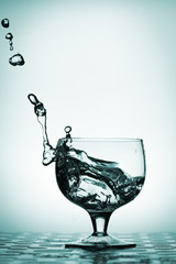 Water splash in glass, columbia blue background.