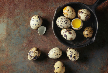 Whole and broken quail eggs with yolk in shell in small iron cast pan over old rusty texture metal...