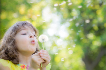 Happy child blowing dandelion flower outdoors