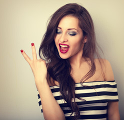 Young happy female model showing rock gesture. Bright makeup and red lipstick. Toned vintage portrait. CLoseup