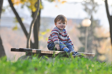 Baby sits on a bench in the park, One year old child outside