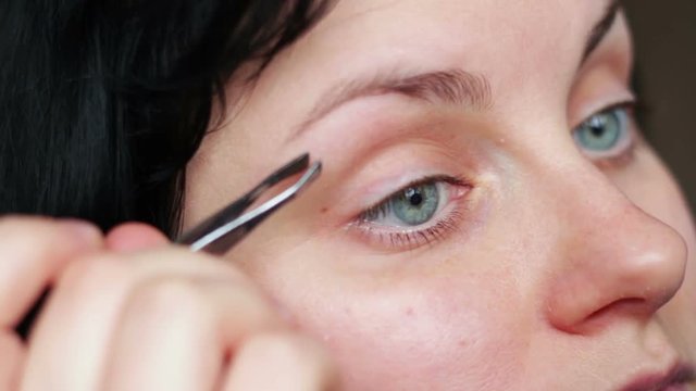 Woman plucking eyebrows depilating with tweezers