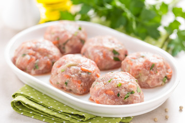 Raw meatballs on white plate, cooking in kitchen