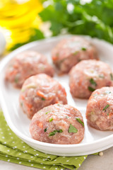 Raw meatballs on white plate, cooking in kitchen
