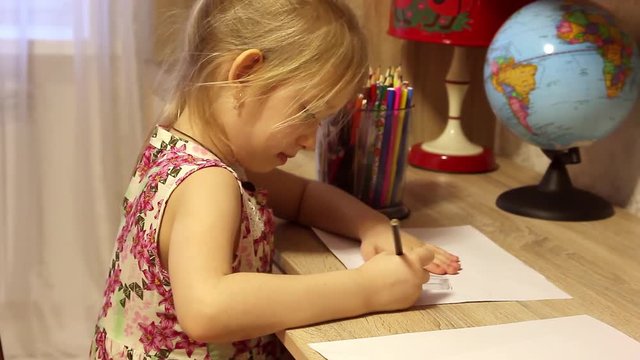 Beautiful little girl is drawing with pencils on paper in his room.