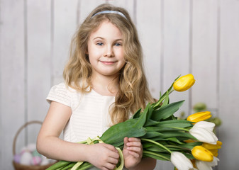 Portrait of cheerful little blonde girl with tulips bouquet on white wood background