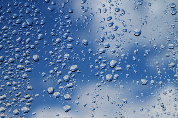 Rain drops on window with blue cloudy sky in background , spring rainy day 