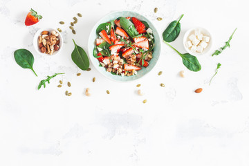 Strawberry salad. Spinach leaves, sliced strawberries, nuts, feta cheese on white background....