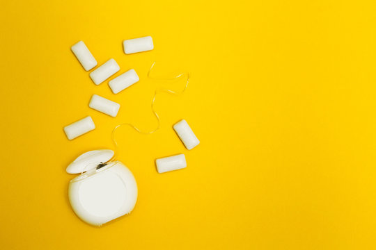 Dental floss and chewing gum cushions on a yellow background.