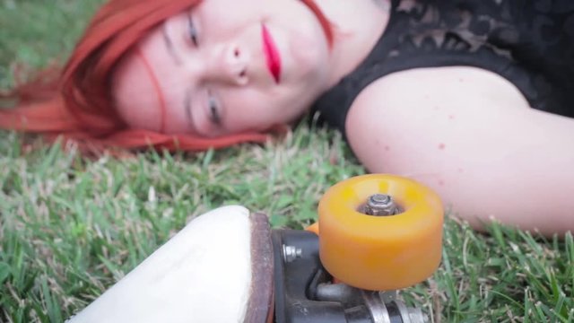 red-haired girl in a black dress lay on the grass next to the skates, skate wheel turns