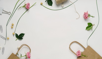 Feminine desk frame with pink roses, green leaves, and gift bags on white background. Flat lay, top...