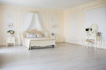 Bedroom in soft light colors. Big comfortable double bed in elegant classic interior
