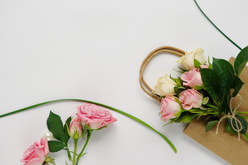 Feminine desk with pink roses, green leaves, and gift bag on white background. Flat lay, top view. Flower background. Women's day, mother's day.