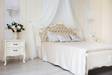 Bedroom in soft light colors. Big comfortable double bed in elegant classic interior