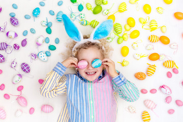 Child on Easter egg hunt. Pastel rainbow eggs.