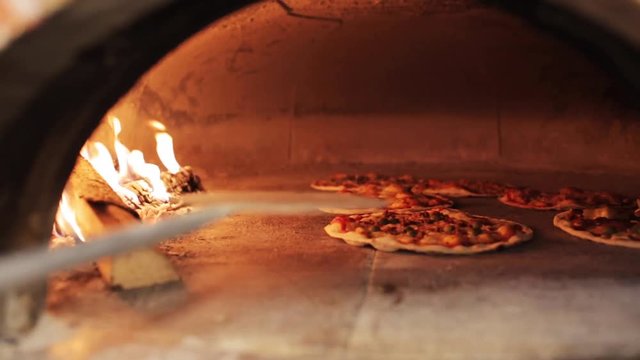 peel placing pizza baking in oven at pizzeria
