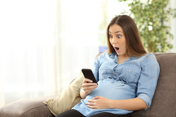 Amazed pregnant woman looking at smart phone