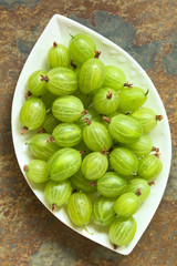 Raw gooseberries (lat. Ribes uva-crispa) on plate, photographed overhead on slate with natural light (Selective Focus, Focus on the gooseberries on the top)