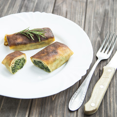 pancakes with spinach on a white plate. cut into pieces. with rosemary. on a wooden table