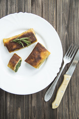 pancakes with spinach on a white plate. cut into pieces. with rosemary. on a wooden table
