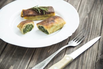 pancakes with spinach on a white plate. cut into pieces. with rosemary. on a wooden table