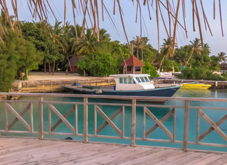 Boat floating on the beautiful tropical beach front of exotic island with turquoise crystal clear water and green palms.