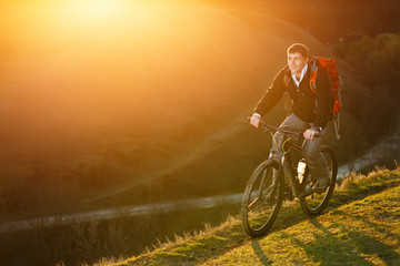 Fototapeta na wymiar Man with red backpack riding on the mountain bicycle on a trail with bright sun on the sunset