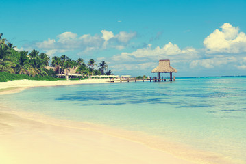 Tropical white sandy beach. Palm leaf roofed wooden pier with gazebo on the beach. Punta Cana, Dominican Republic