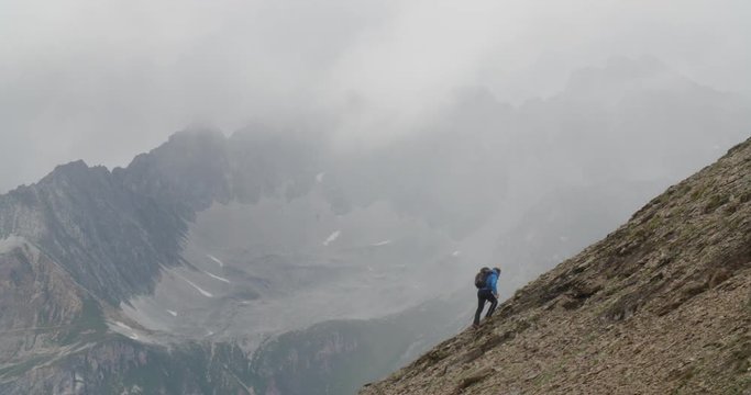 Man hiking up steep mountains with dark clouds.
